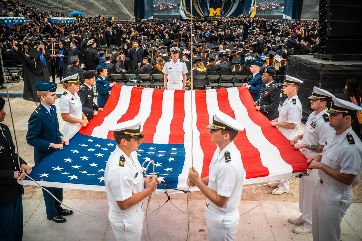 Color guard presenting a large American flag at a stadium graduation ceremony