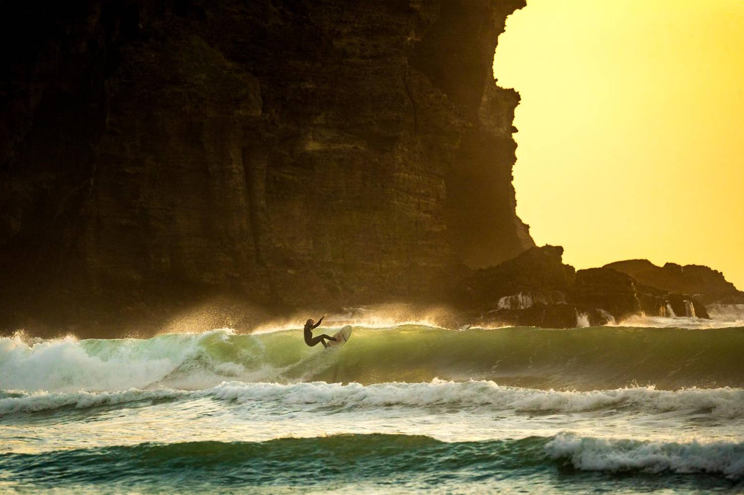 Surfer riding a wave at sunset beneath cliffs