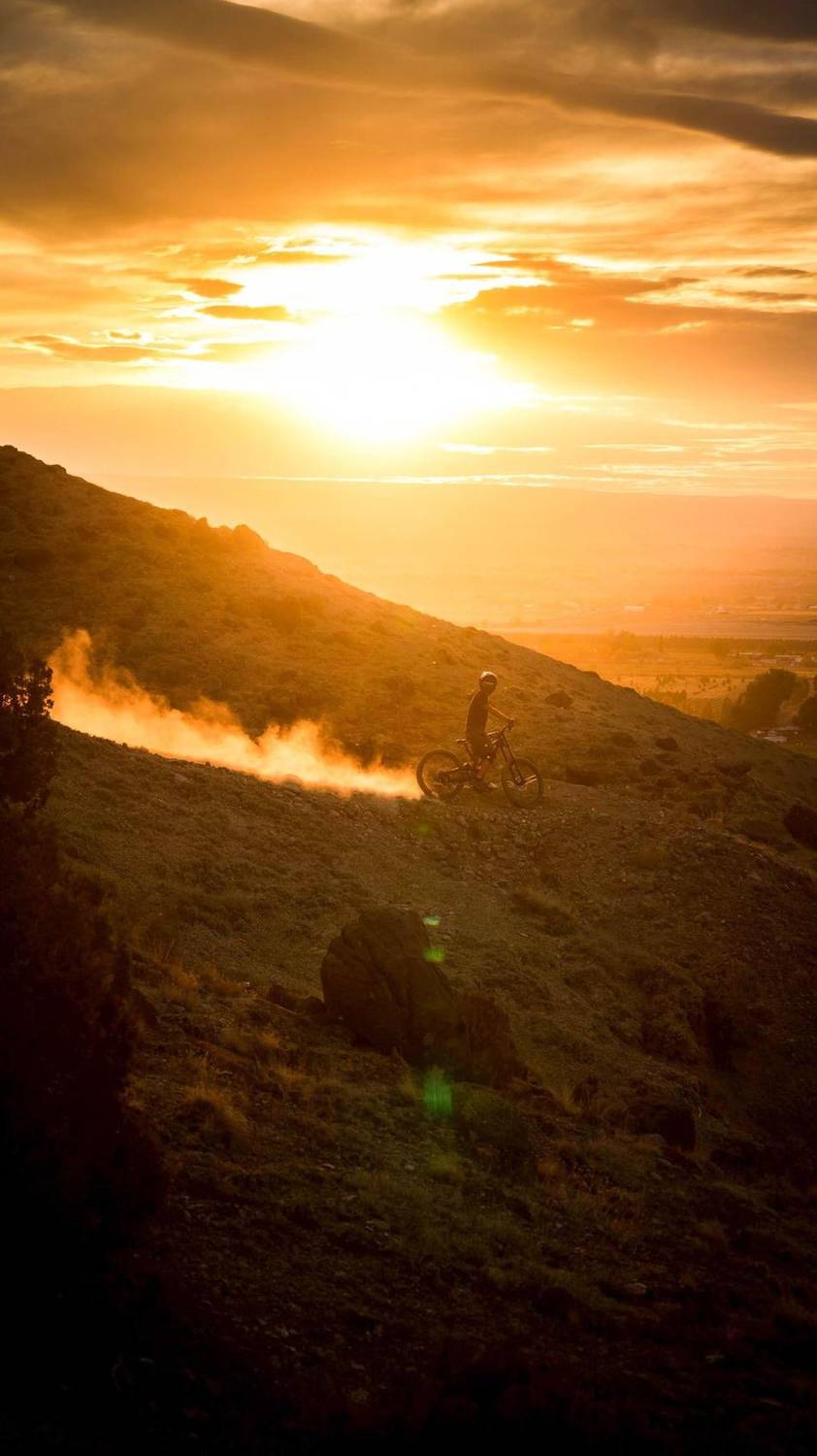 Mountain biker kicking up trail dust on a hillside at sunset