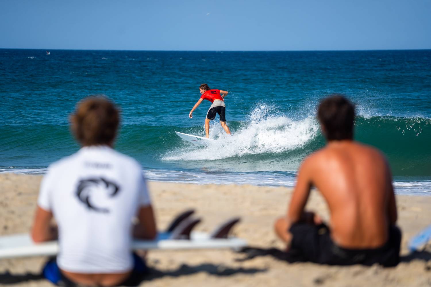 Surfer riding a wave watched by two people on the beach