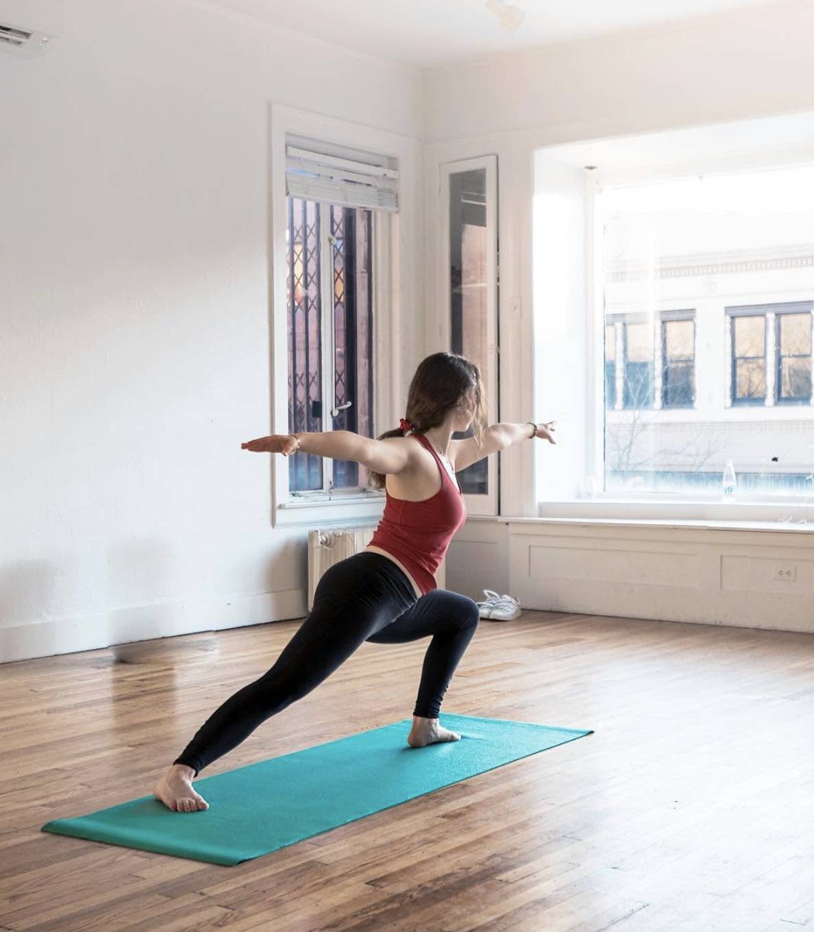 Woman holding warrior II pose in a sunlit room