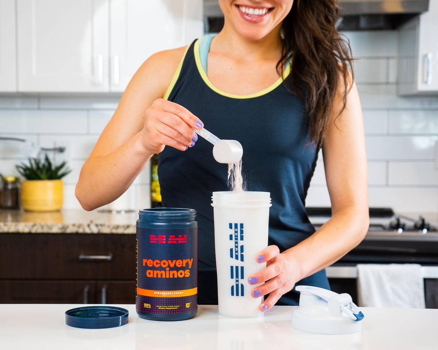 Woman scooping BEAM recovery amino powder into a shaker cup