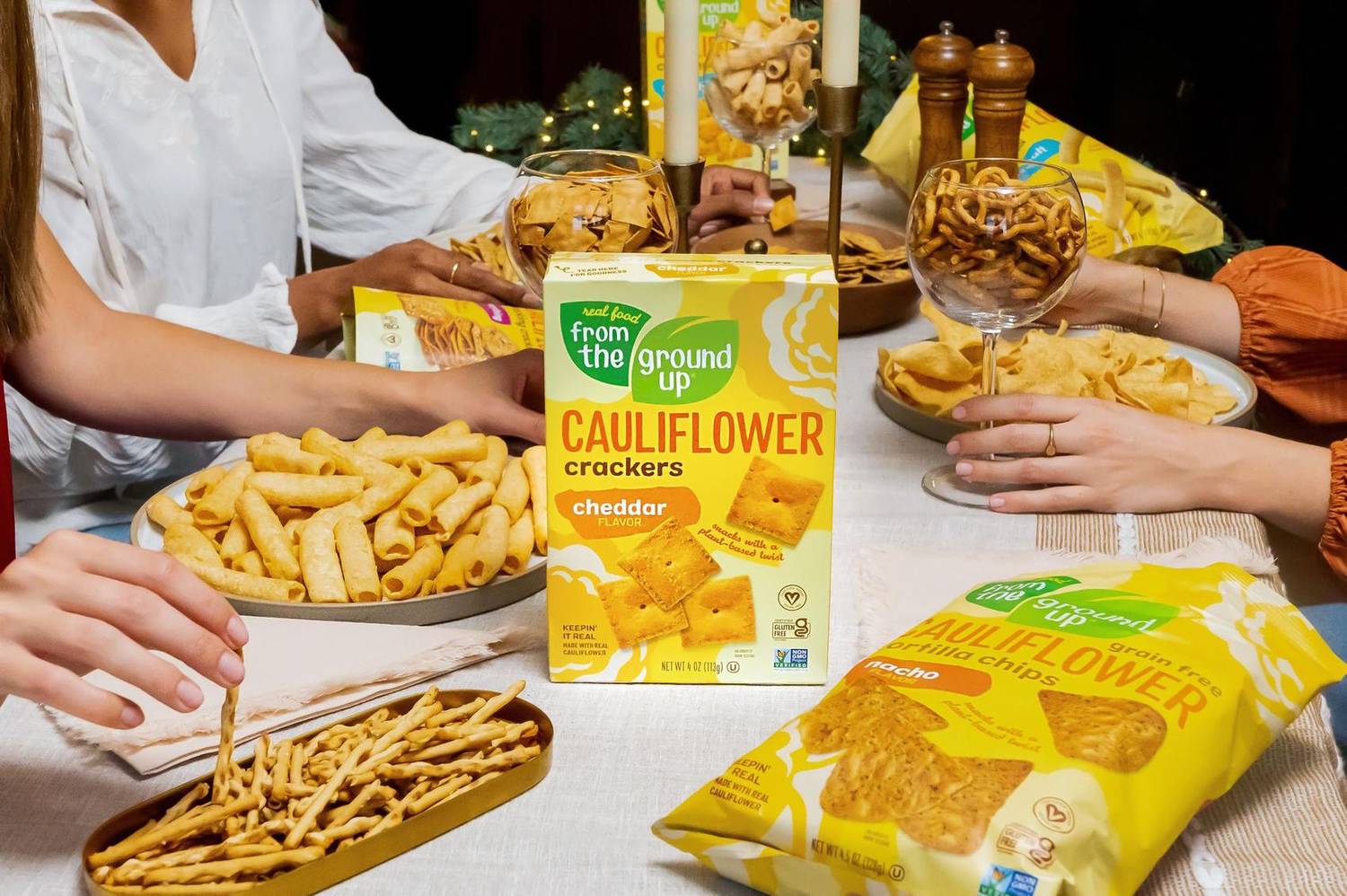 Guests reaching for cauliflower crackers at a candlelit dinner table