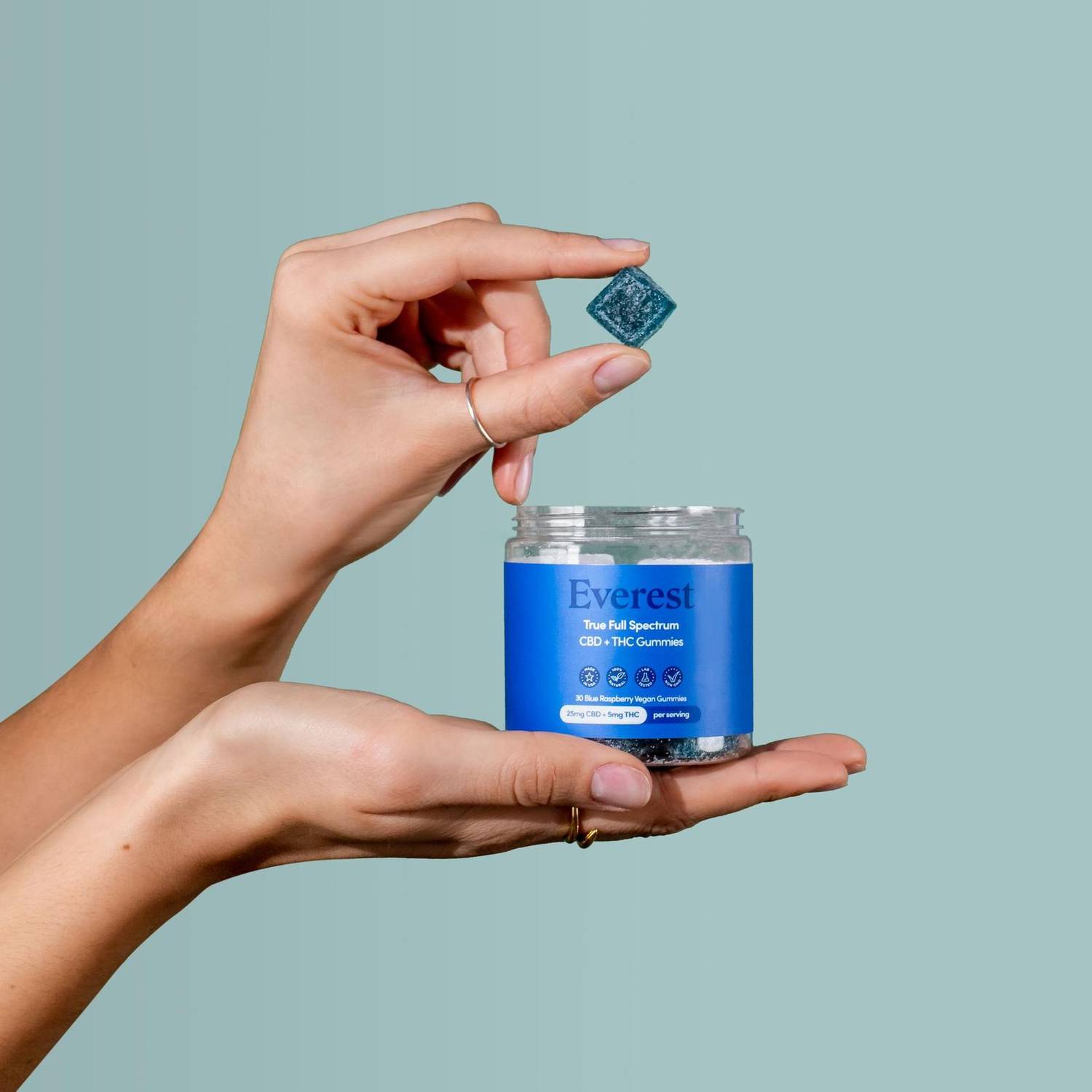 Hand holding a CBD gummy above the jar