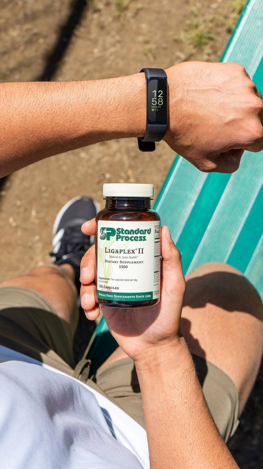 Hand holding a Standard Process supplement bottle outdoors