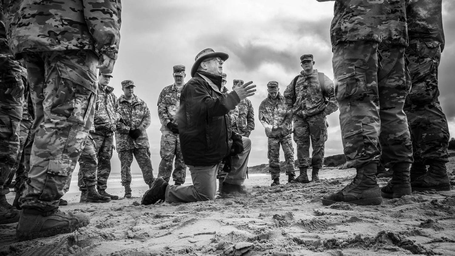 Black and white photo of a speaker addressing soldiers gathered on a beach