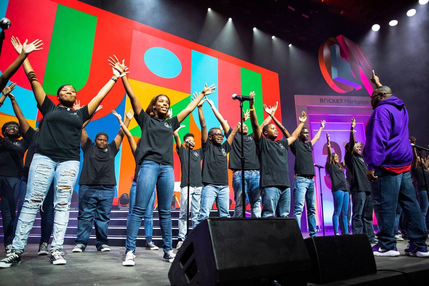 Youth choir raising their hands while performing on stage at a corporate event
