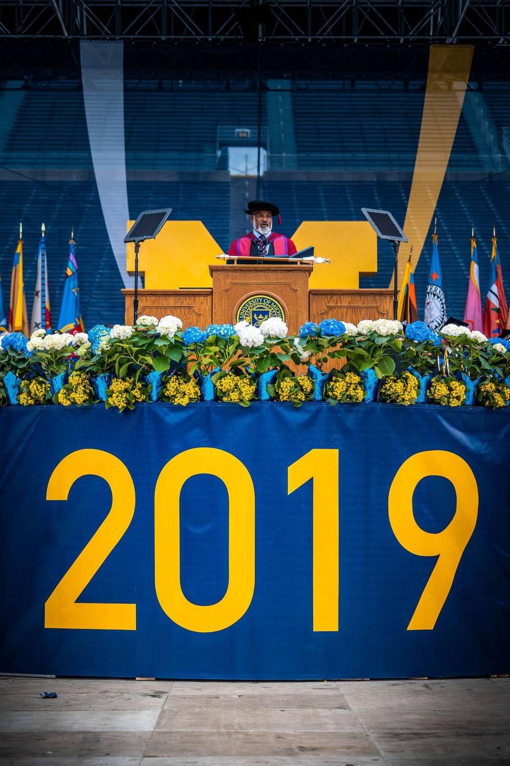 Speaker addressing graduates from a podium with a large '2019' banner