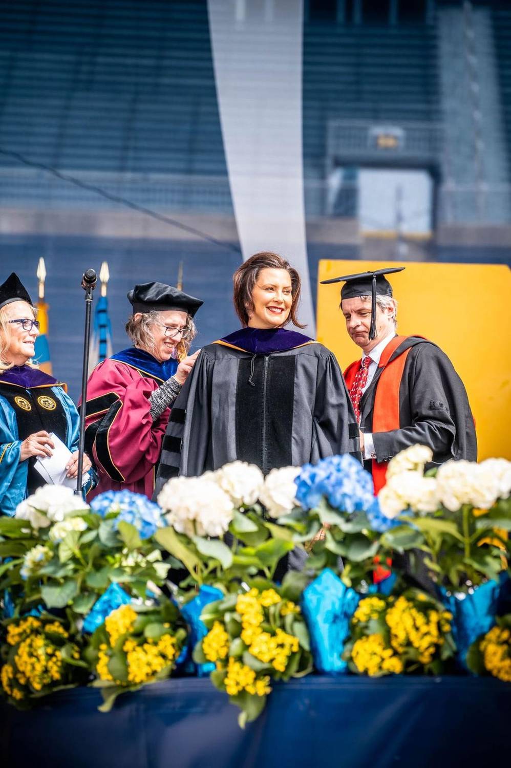 Dignitaries in academic regalia smiling together on stage at a commencement ceremony