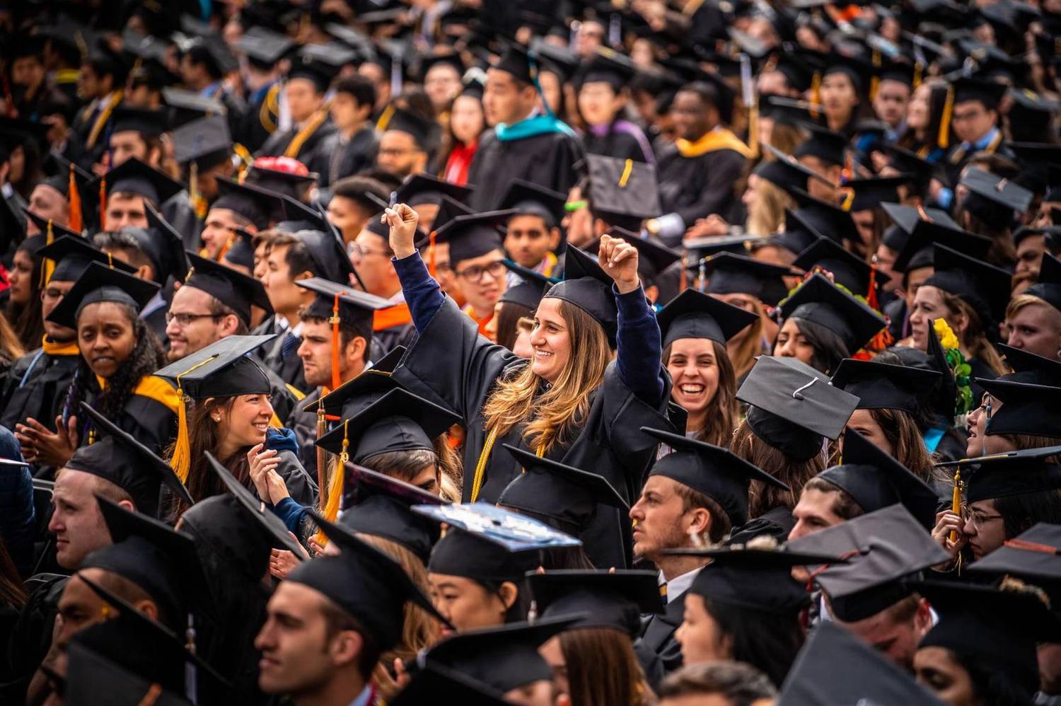 Graduates cheering with raised fists in a packed stadium crowd