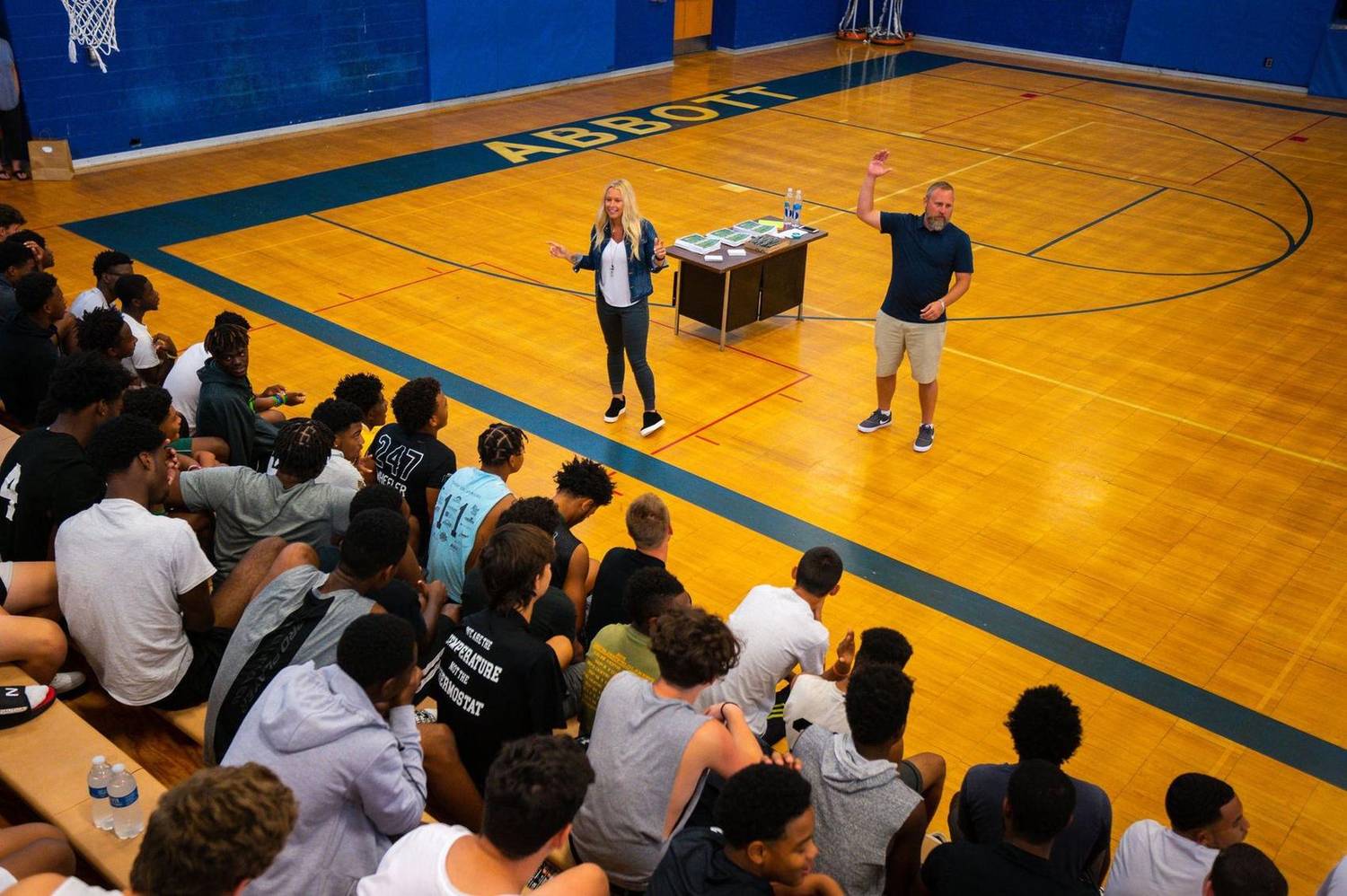 Speakers addressing a group seated in gym bleachers