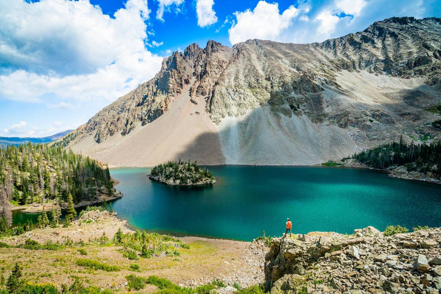 Hiker overlooking a turquoise alpine lake with a tree-covered island