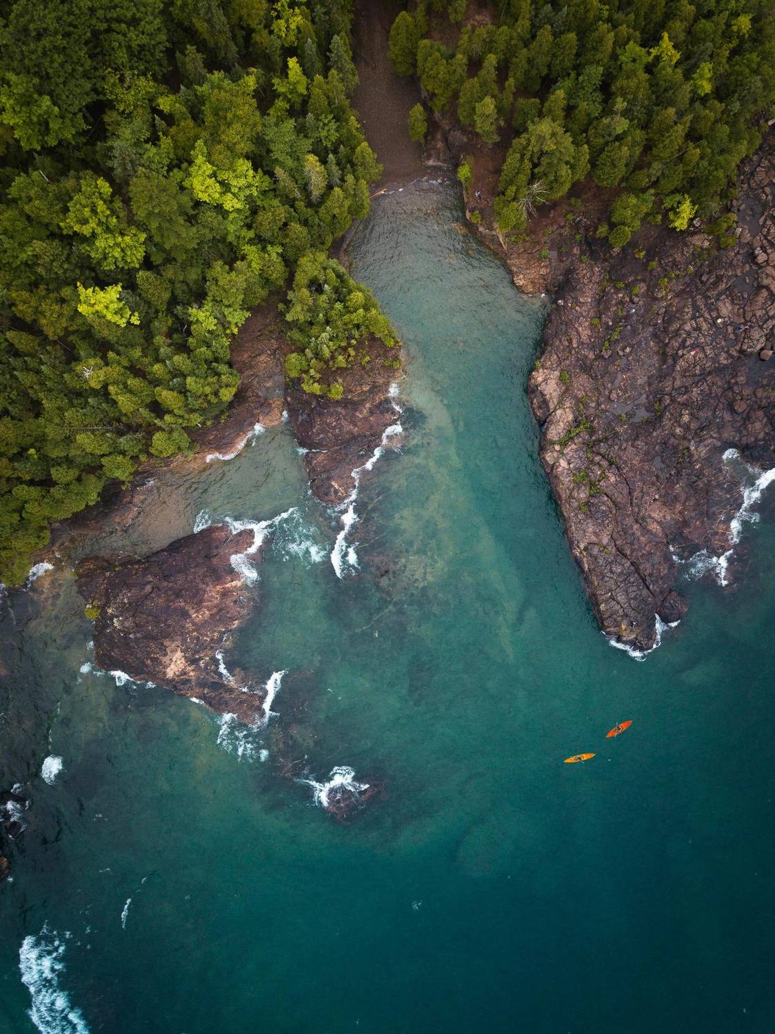 Aerial view of kayakers in a turquoise rocky cove