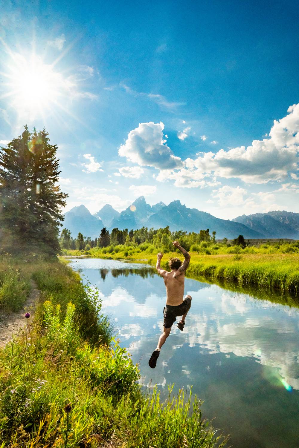 Man leaping into a river with mountains in the background