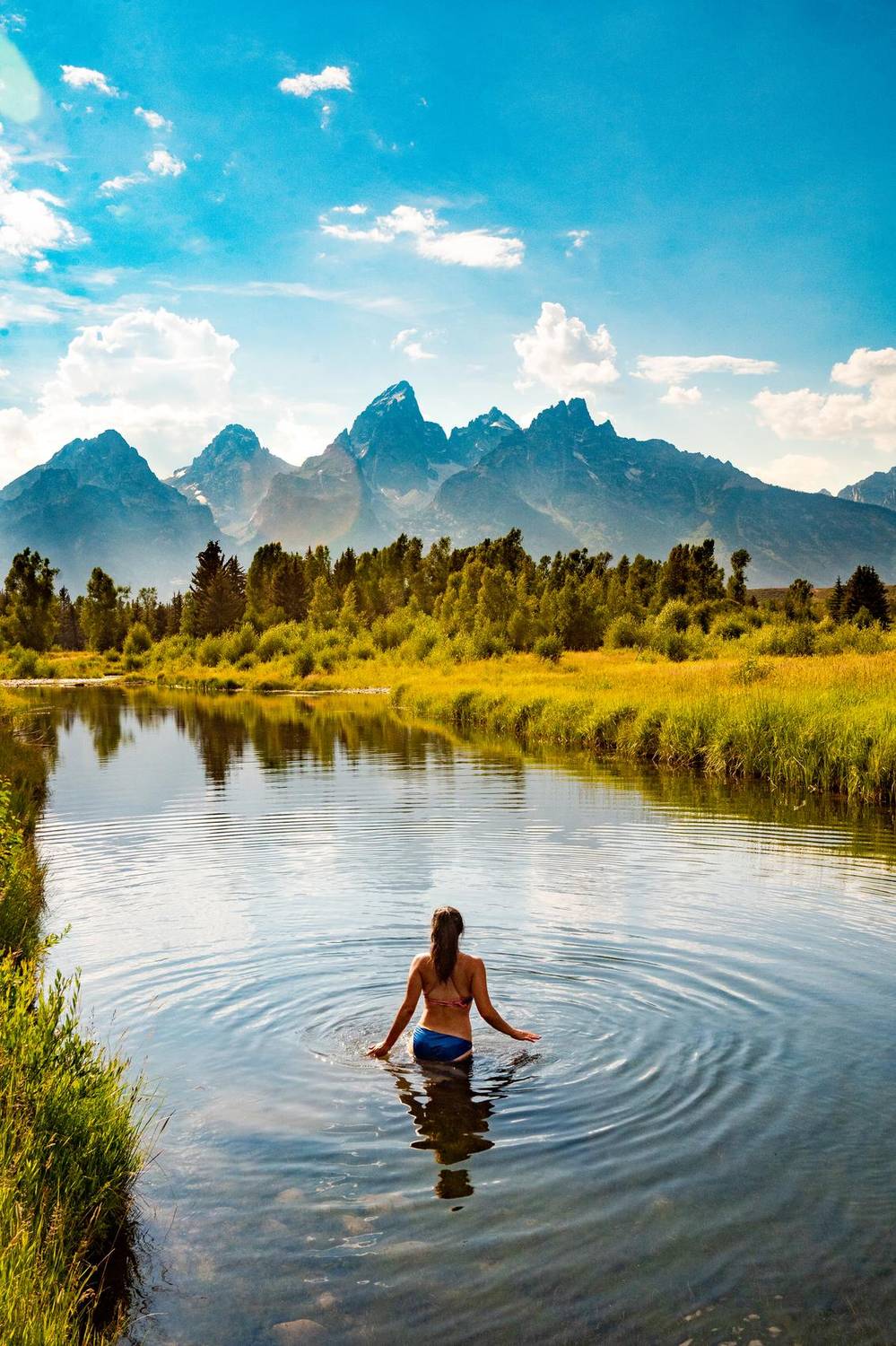Woman wading into a river with the Teton mountains behind her