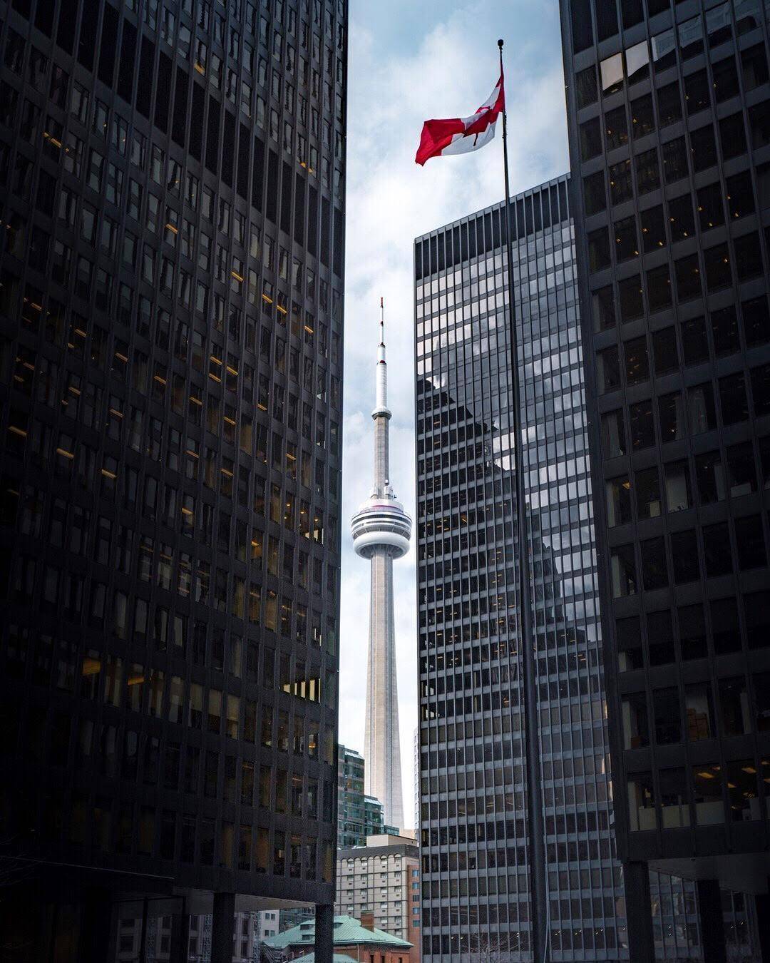 CN Tower framed between skyscrapers with a Canadian flag flying