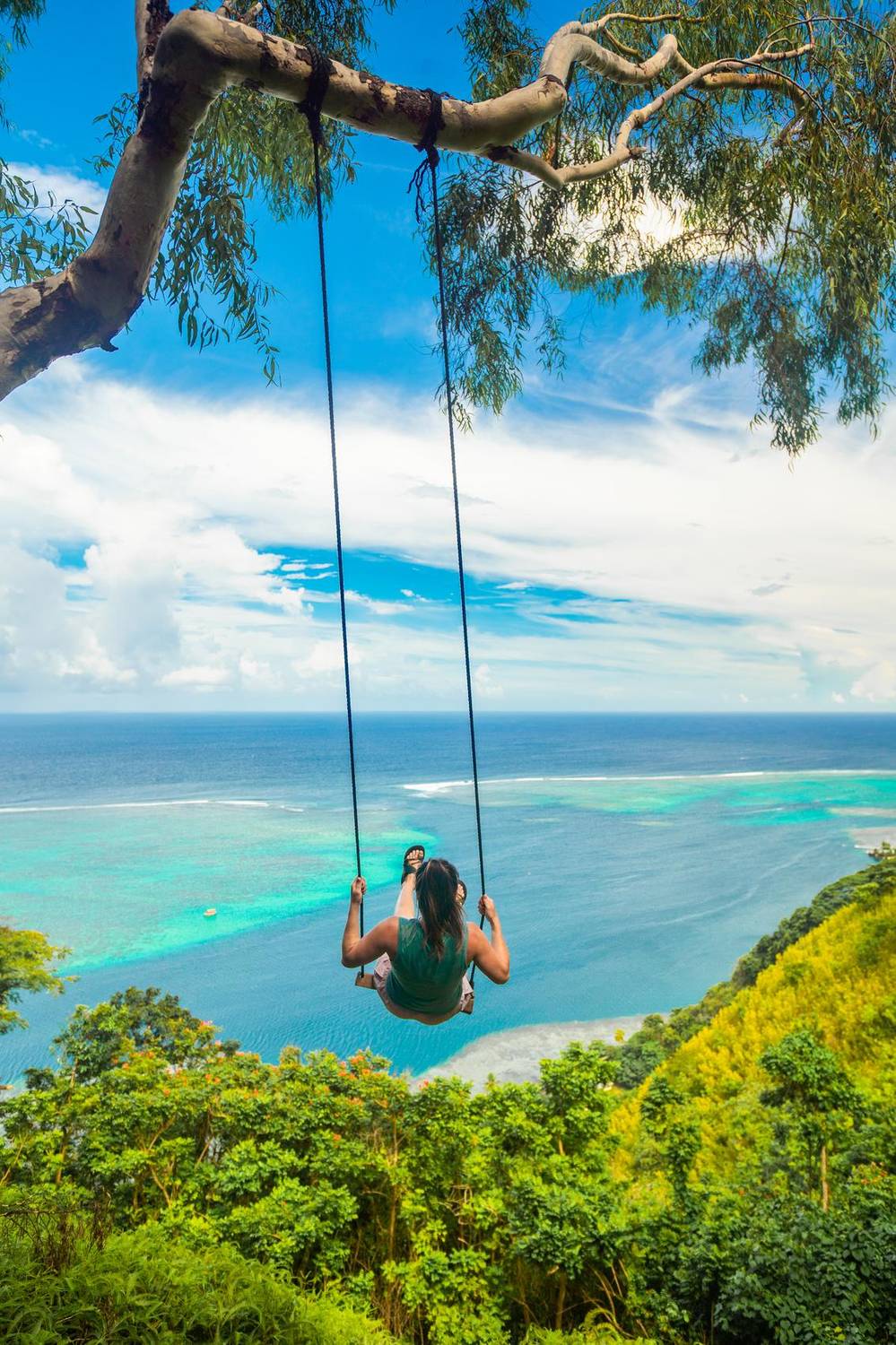 Woman on a rope swing overlooking a turquoise lagoon